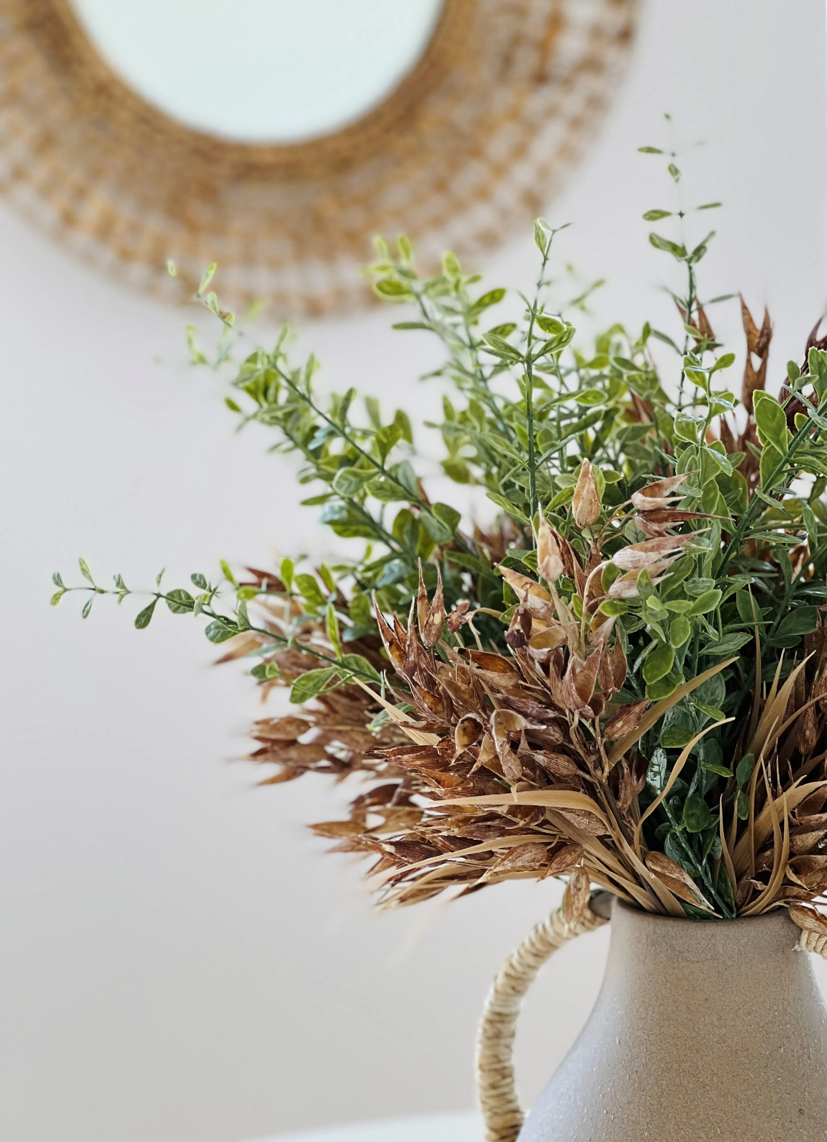Styling detail with dried botanicals in ceramic pitcher and woven mirror
